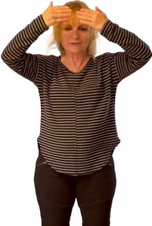 Woman elbows bent, holding hands in front of forehead in Qi Gong pose.